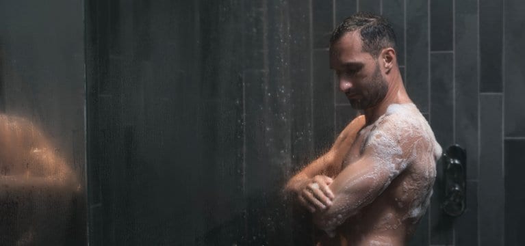 Athletic man lathering and exfoliating his skin in grey slate tiled shower.