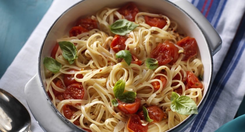 Spaghetti noodles in a bowl with tomatoes and green garnish
