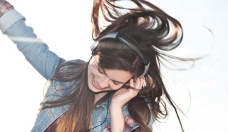 Una mujer con pelo brillante bailando con audífonos para ilustrar la página de shampoo Sedal