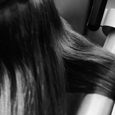 Close up of a model having a section of her hair curled in curling tongs.