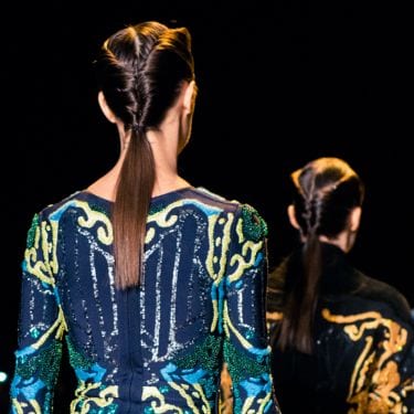 Photo of a models on the catwalk with their back to the camera, wearing colourful dresses with their hair in ponytails